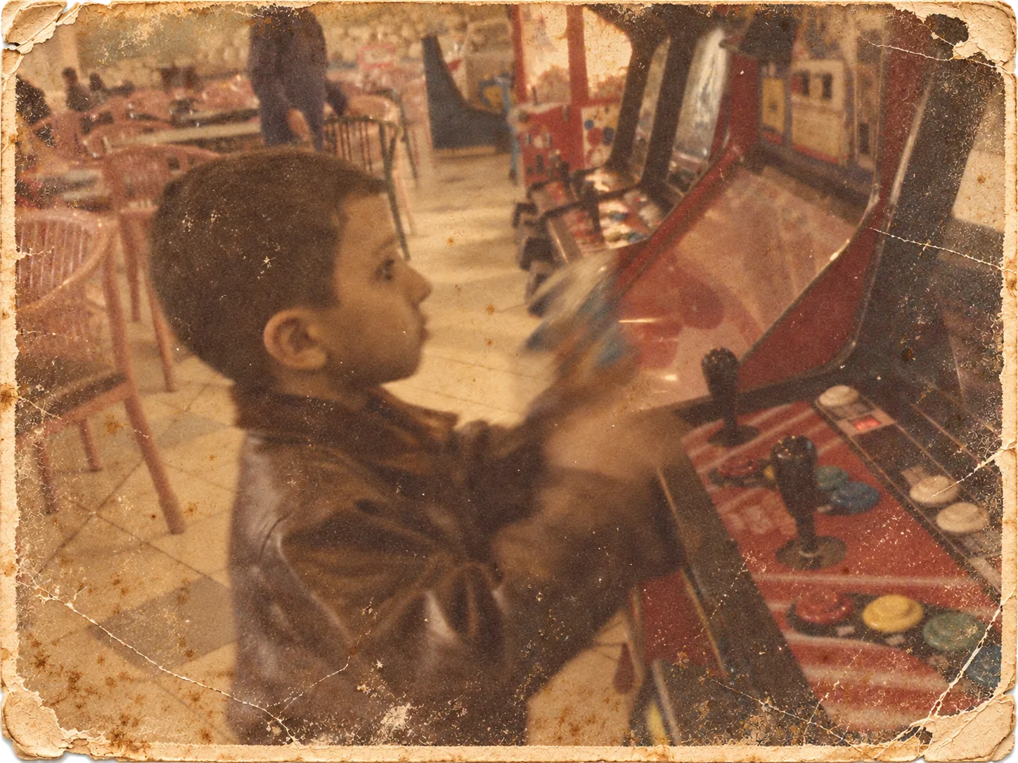 Mansy as a small boy in a leather jacket, playing an arcade cabinet, in an old worn photograph